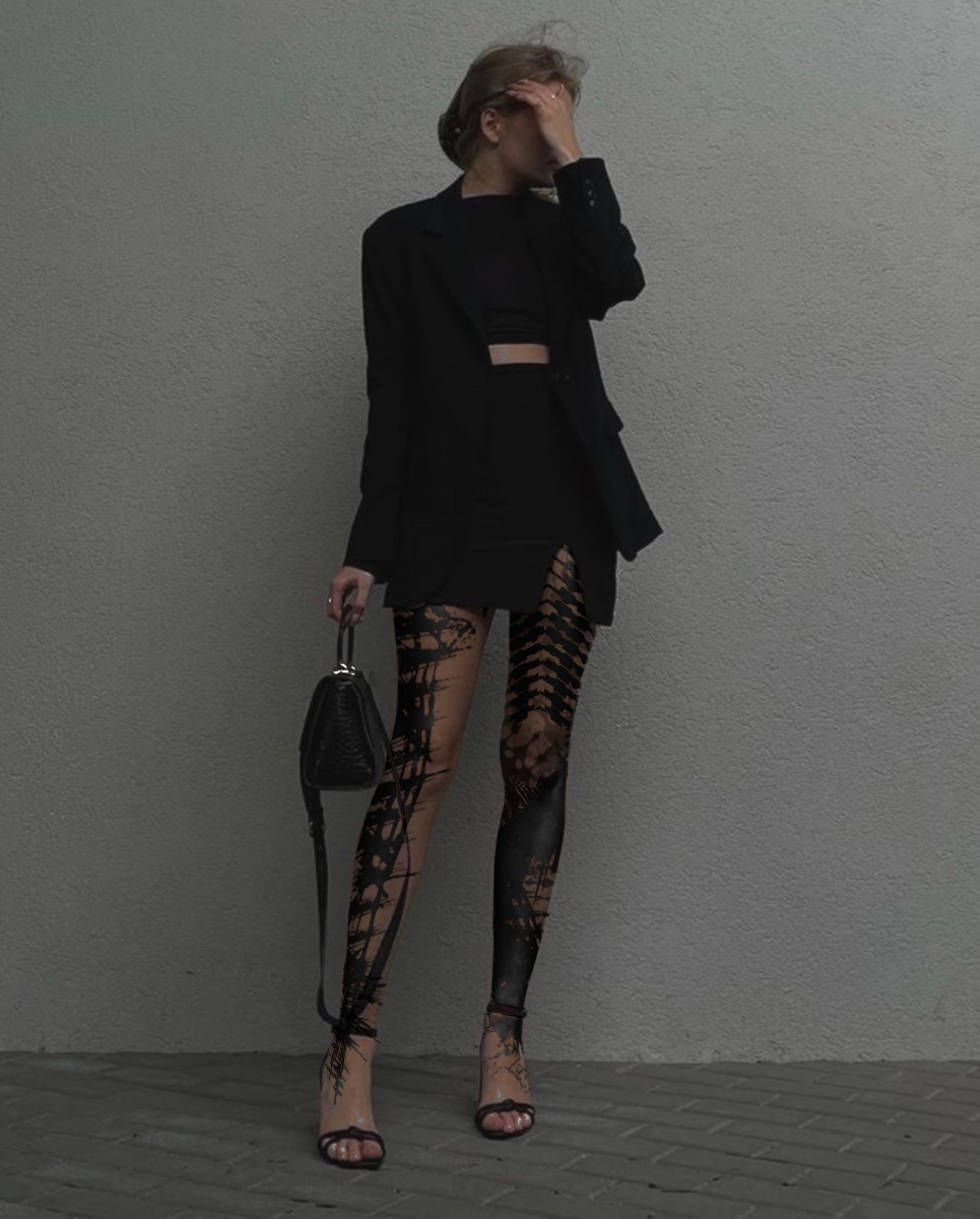 Ganzfigur auf Pflaster vor einer grauen Wand, mit Blackwork an beiden Beinen bis zu den Füßen.