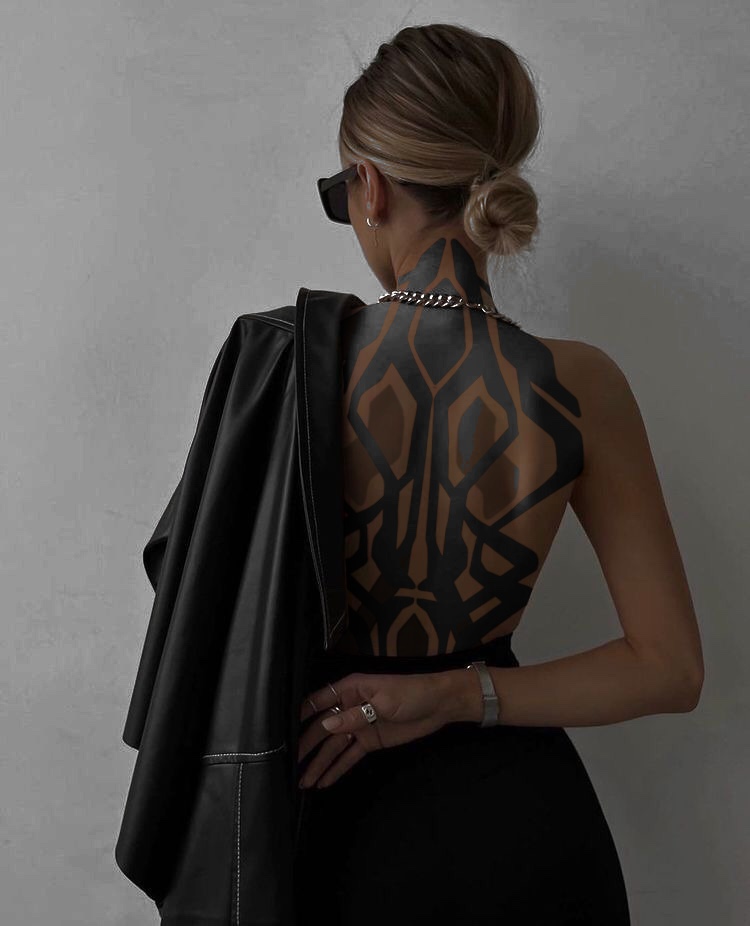 Rückansicht bis zur Taille vor einer grauen Wand, mit geometrischem Blackwork über den ganzen Rücken und den Hals.