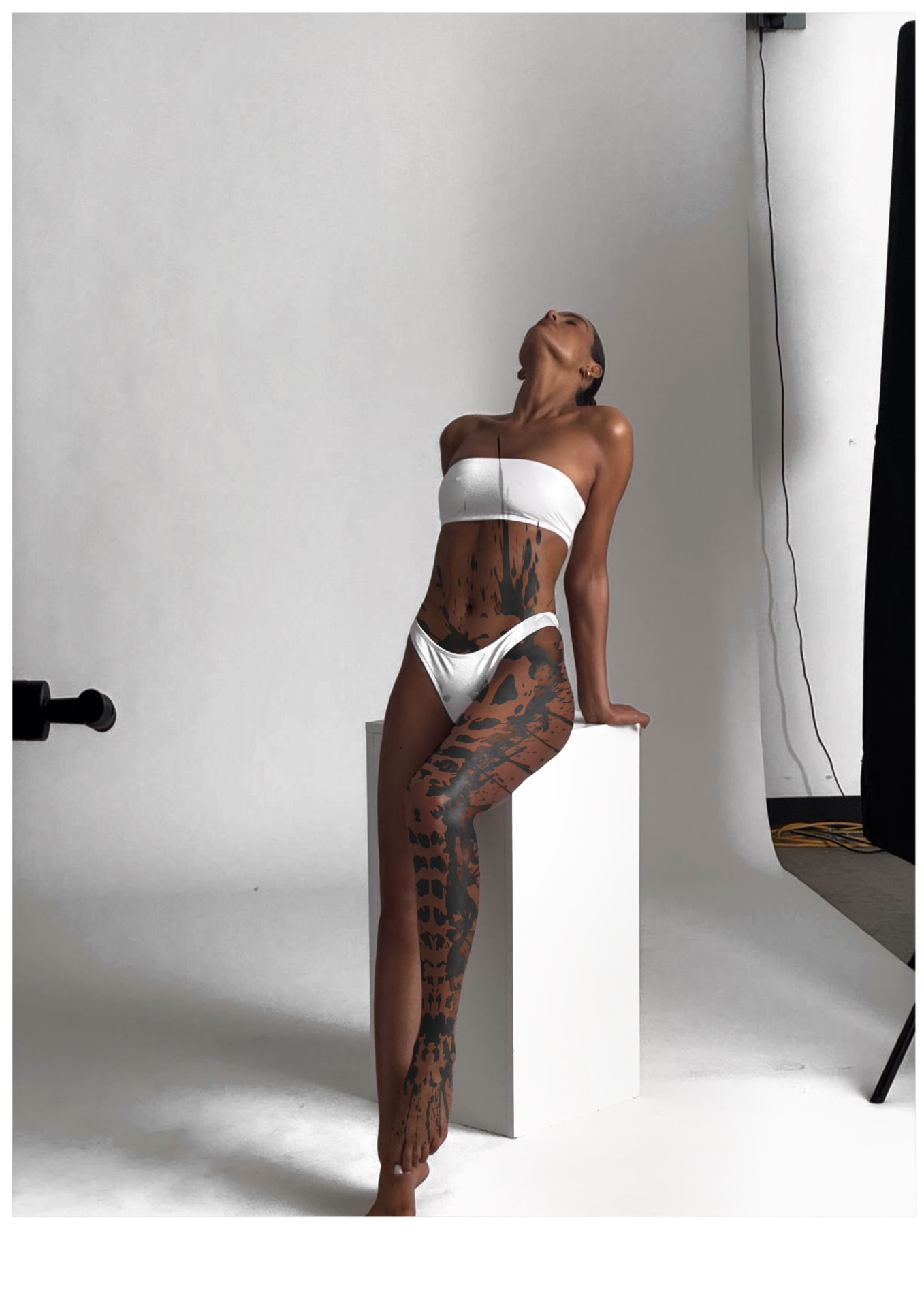 Ganzfigur in einem weißen Studio-Zyklorama, mit Blackwork an gespritzten Rändern über Bauch, linker Hüfte und linkem Bein.